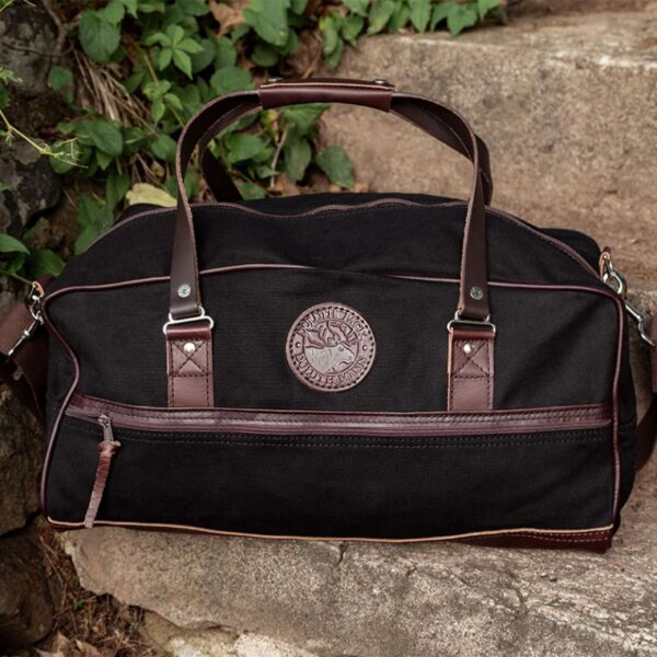 A Black Color Duffle Bag With Brown Strap on Stone